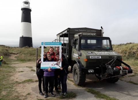 Volunteers from Yorkshire Wildlife Trust stood in front of Spurn lighthouse with the Unimog vehicle