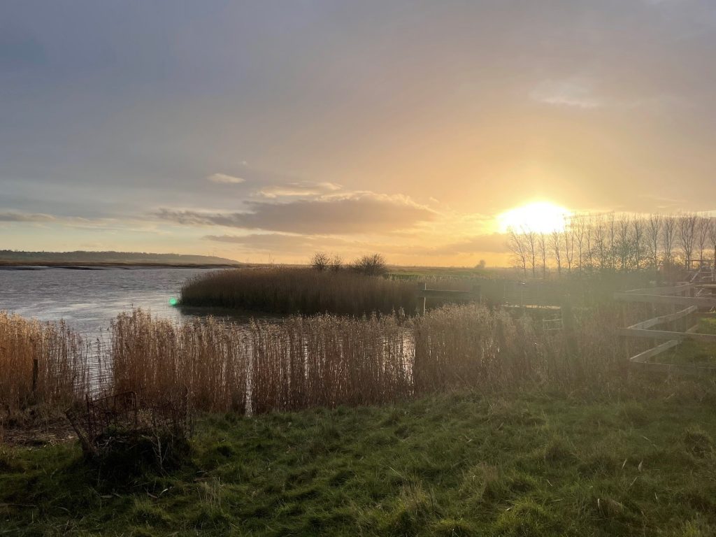 The sun shines brightly on the horizon over a view looking west towards Trent Falls from the bridge crossing the Market Weighton canal near Broomfleet